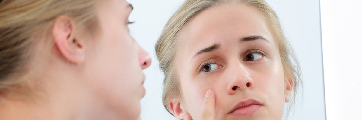 Teenage girl checking her face for pimple in the mirror