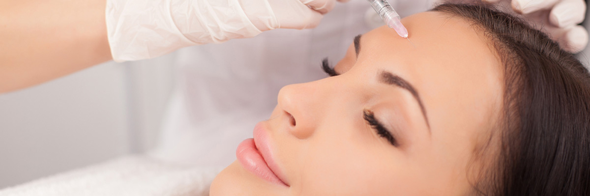 Close up of hands of expert beautician injecting botox in female forehead