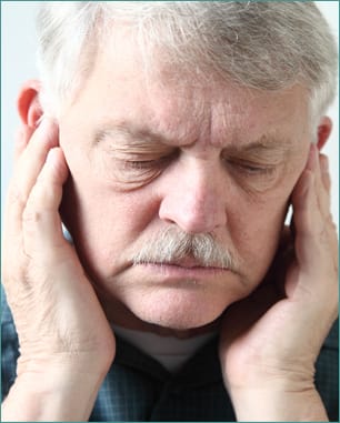 Older man holds both hands to his upper jaw near the ears.