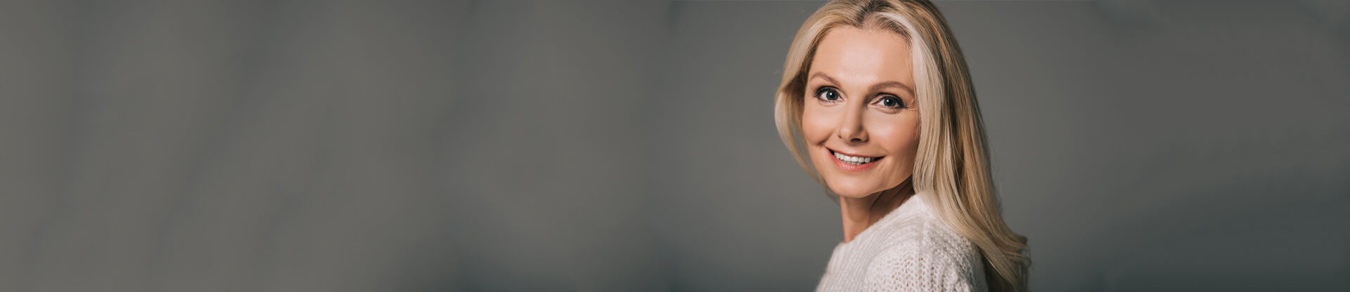 Beautiful mature woman in white sweater isolated on grey
